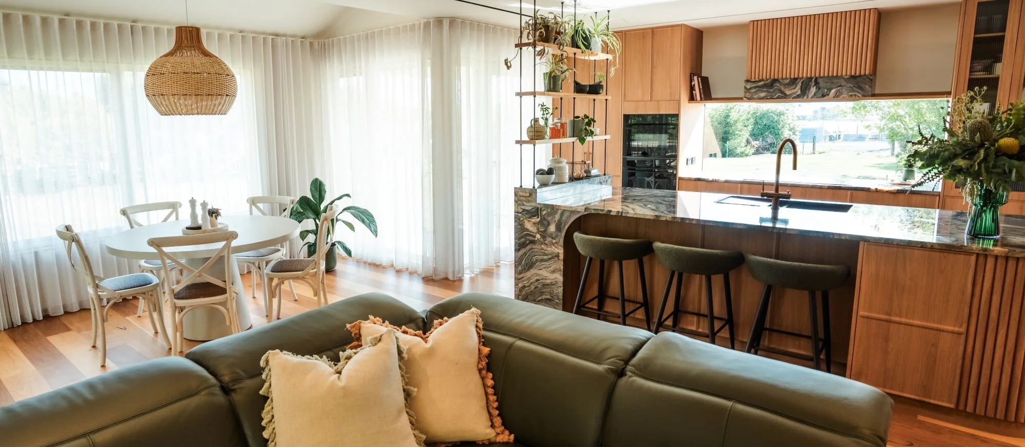 Open plan living and kitchen space at Raeburn connecting timber joinery, stone surfaces and garden views.