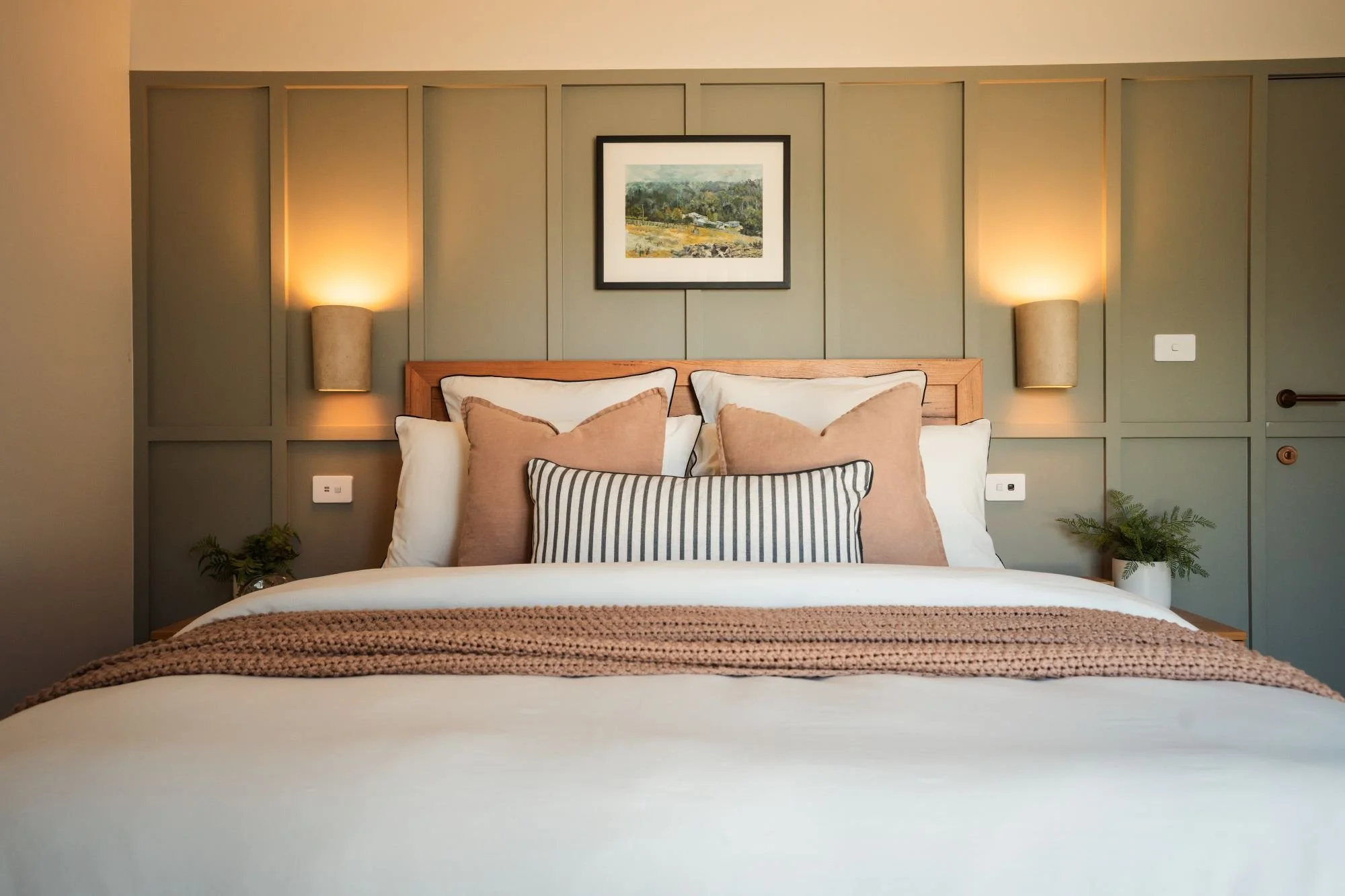 Master bedroom at Raeburn featuring panelled wall detail, soft lighting and layered bedding.
