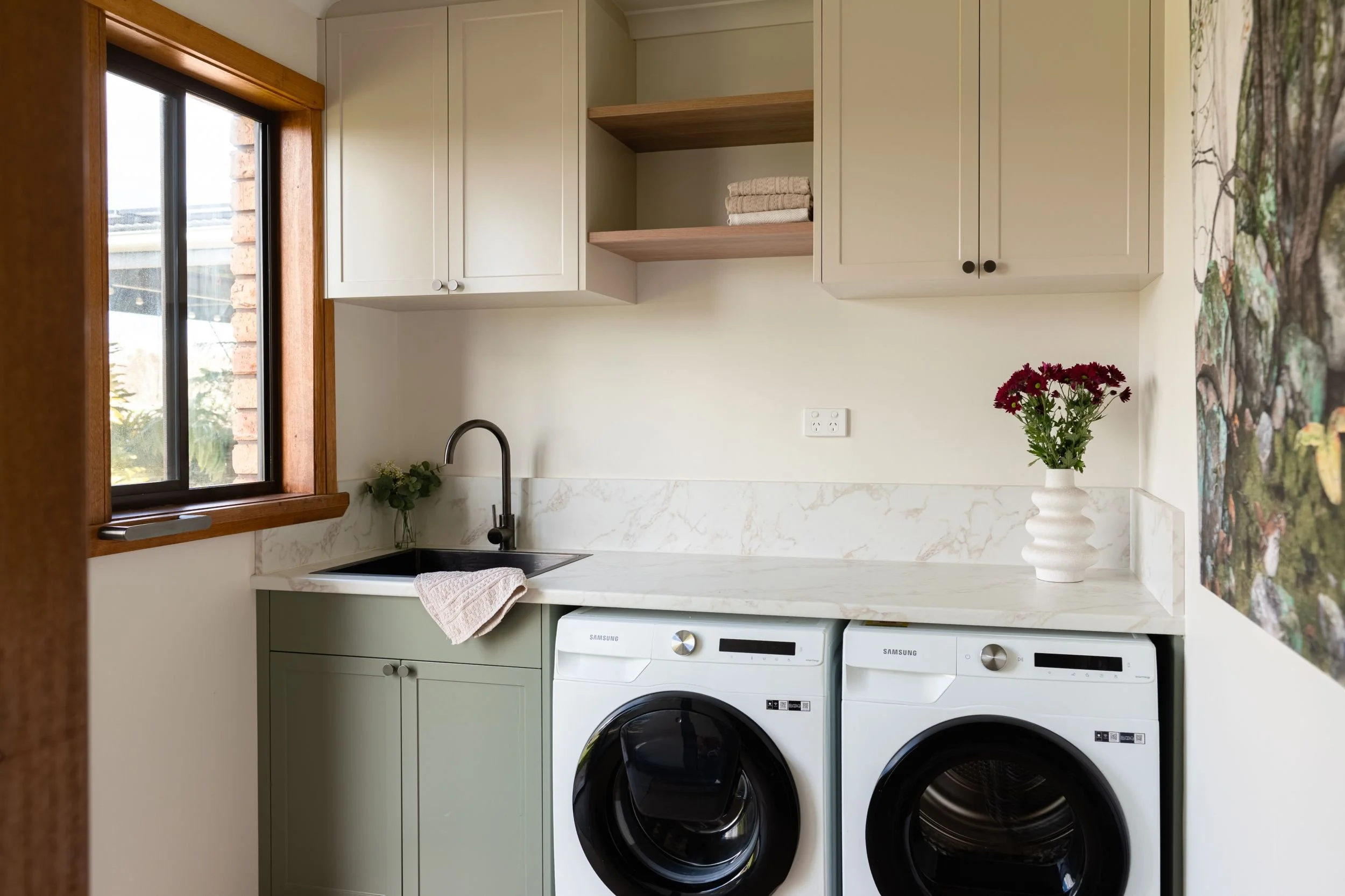 Laundry with sage cabinetry, marble-look splashback and front-loader washer and dryer
