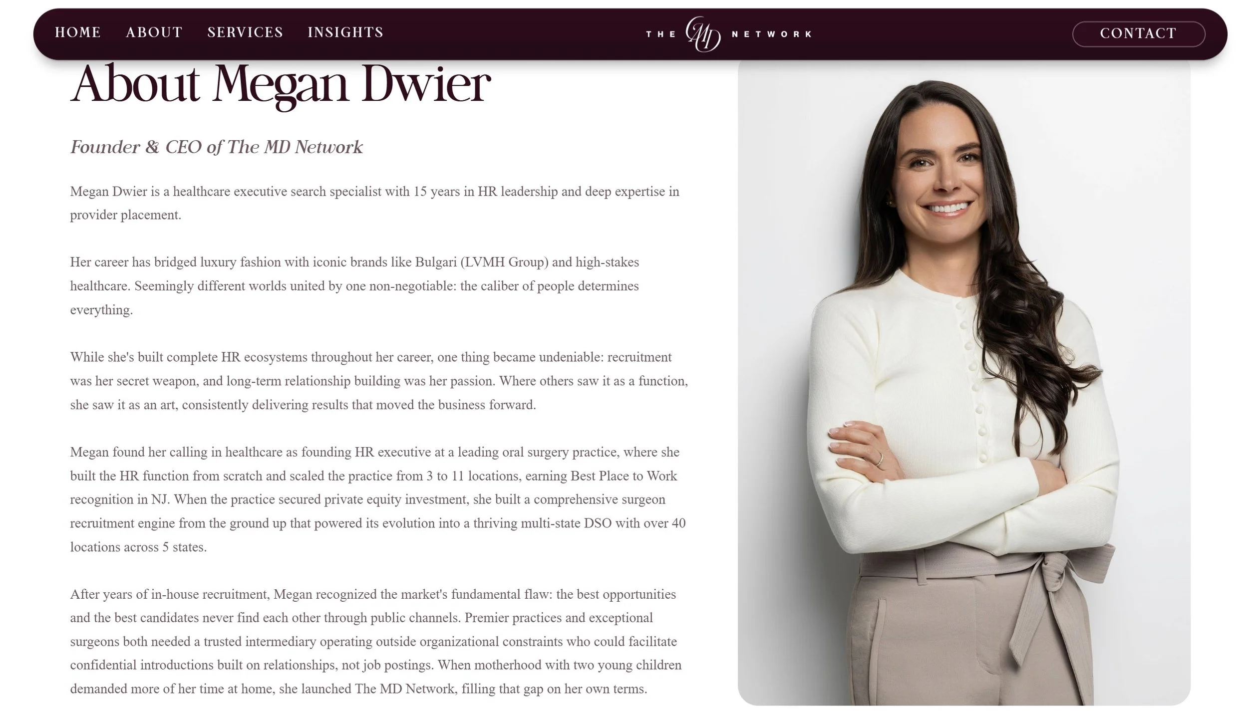 Professional woman with long dark hair smiling, standing with arms crossed, wearing a white sweater and beige pants.