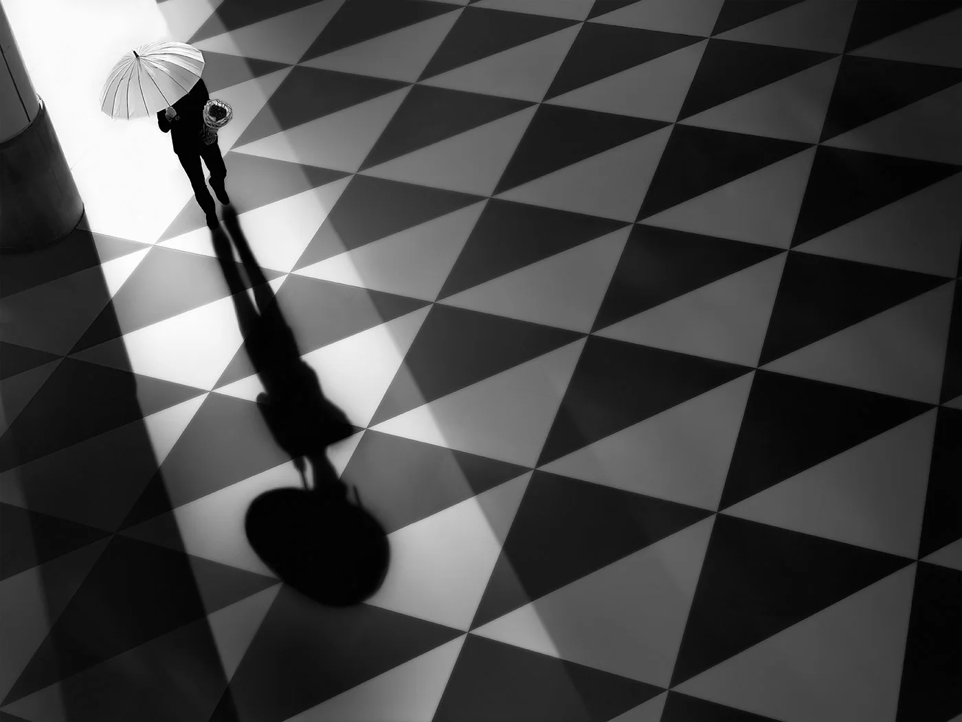 A person walking with an umbrella on a patterned floor, casting a shadow.