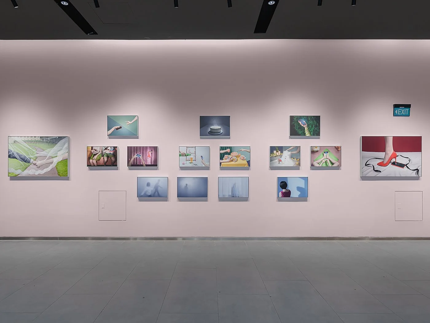 Installation view of A Modern Day Affair exhibition under In Our Own Frame curated by DECK Photography Art Centre. Wide view of a pale pink exhibition wall with fifteen framed photographs arranged in rows.