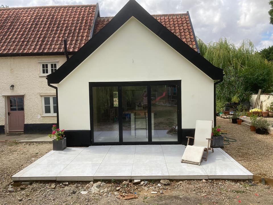 Modern house extension with sliding glass doors, white exterior walls, and a small patio with a lounge chair and potted plants.