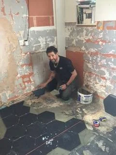 Person installing hexagonal floor tiles in a room under renovation