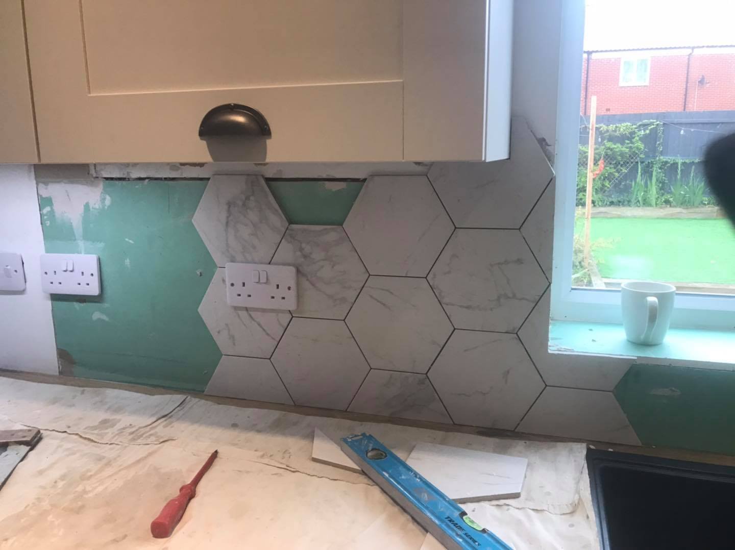Kitchen backsplash with hexagonal tiles, a window, and a countertop with tools and a mug.