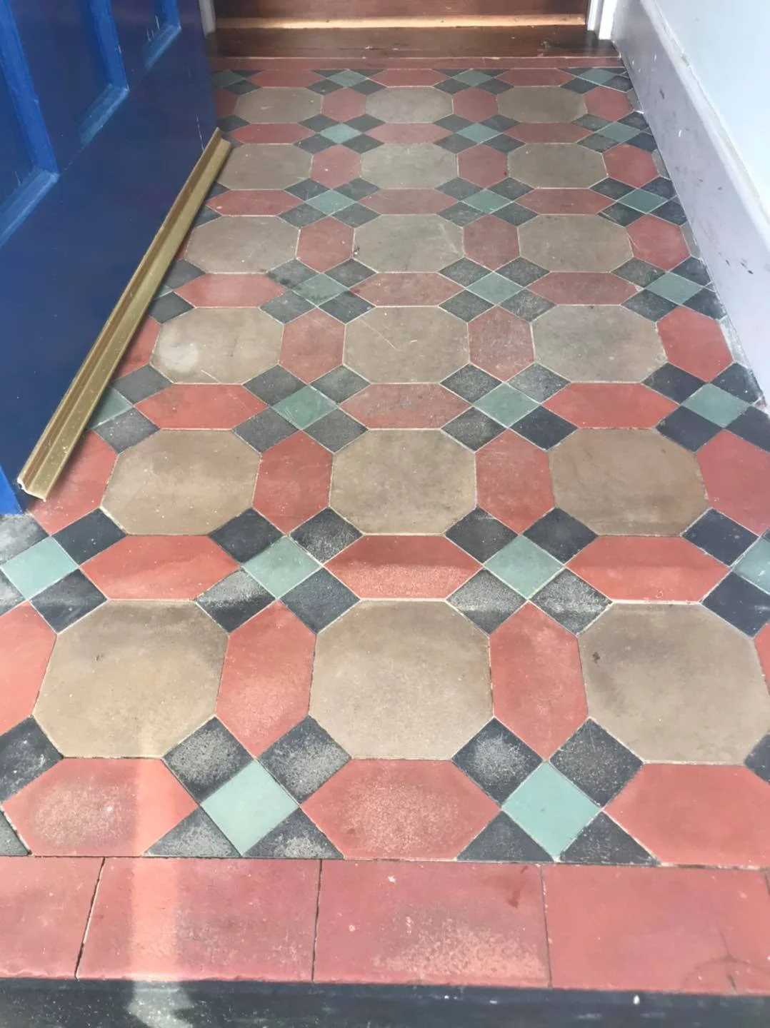 Victorian-style tiled floor with red, green, beige, and black geometric pattern next to a blue door.