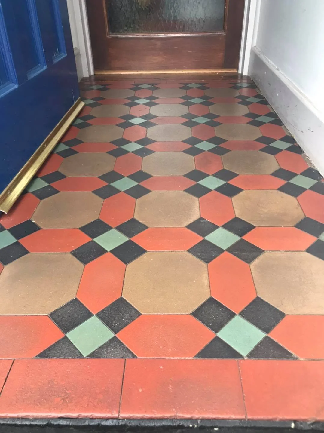 Geometric patterned floor tiles in red, black, and beige in a hallway with a blue door and wooden door.