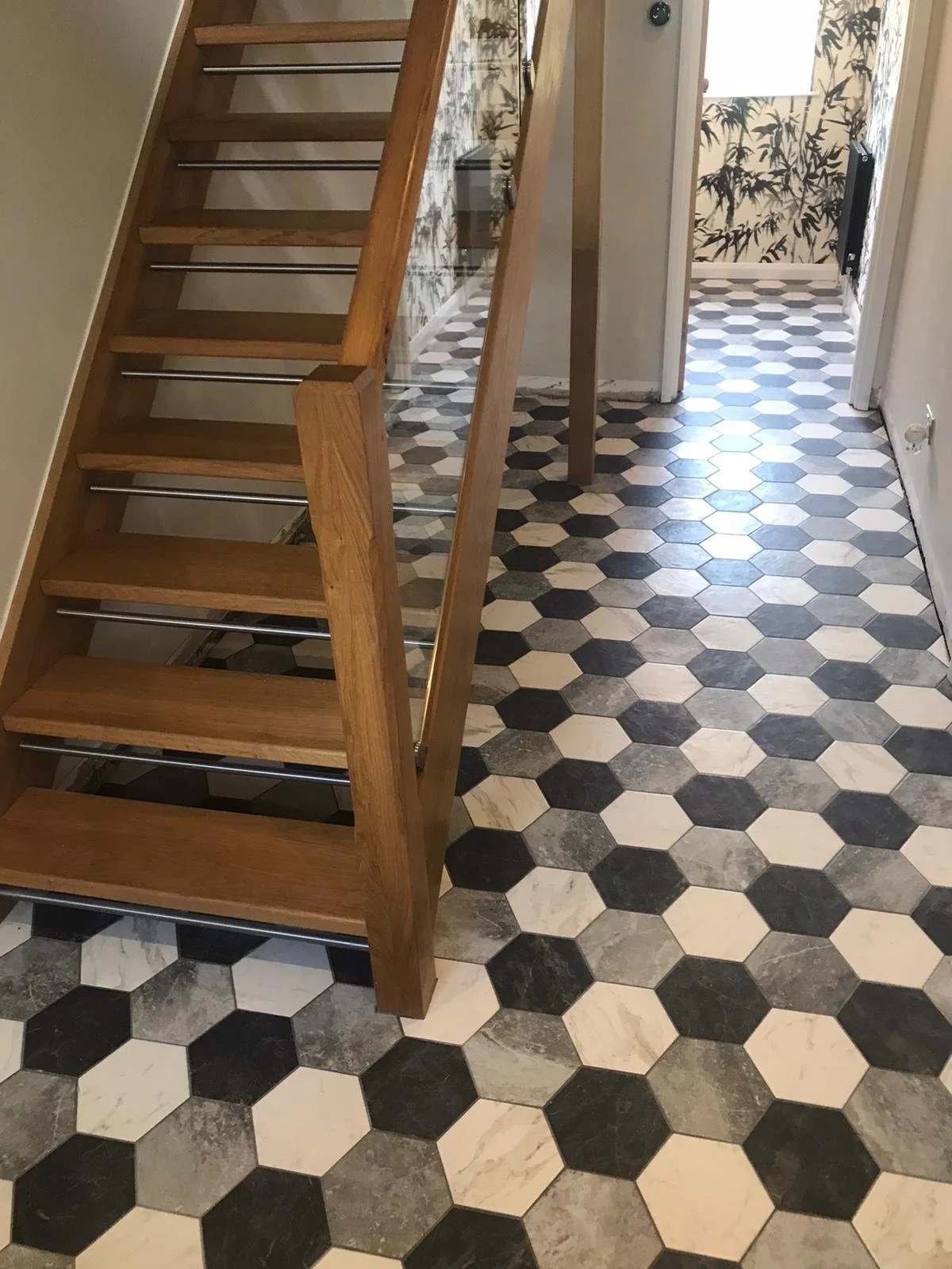 Interior view of staircase with wooden steps, glass railing, and hexagonal black and white patterned tile flooring.