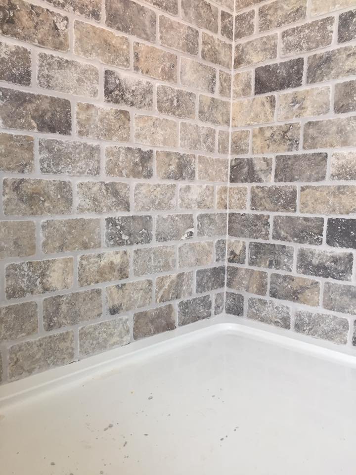 Bathroom corner with stone tile wall and white shower basin.