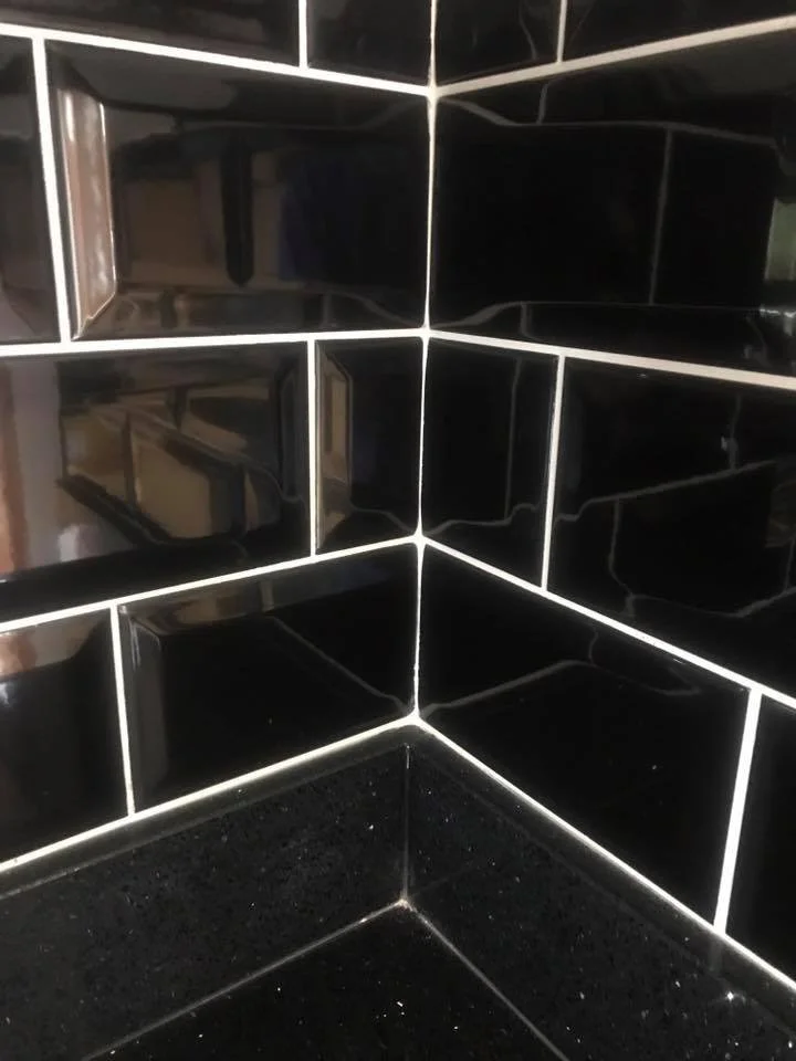 Corner of room with glossy black subway tiles and black countertop