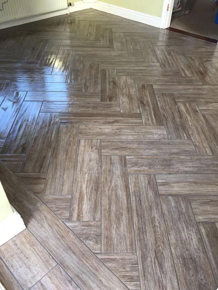 Herringbone pattern wood-look tile flooring in a room with pale green walls and white trim.