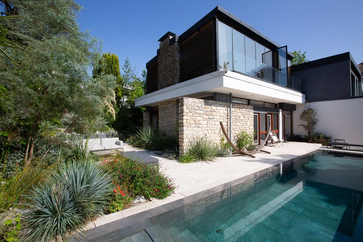 Vue d’un jardin contemporain à Saint-Cloud avec piscine, terrasse en pierre claire, plantations graphiques et aménagement paysager sur-mesure par Simonson Landscape.