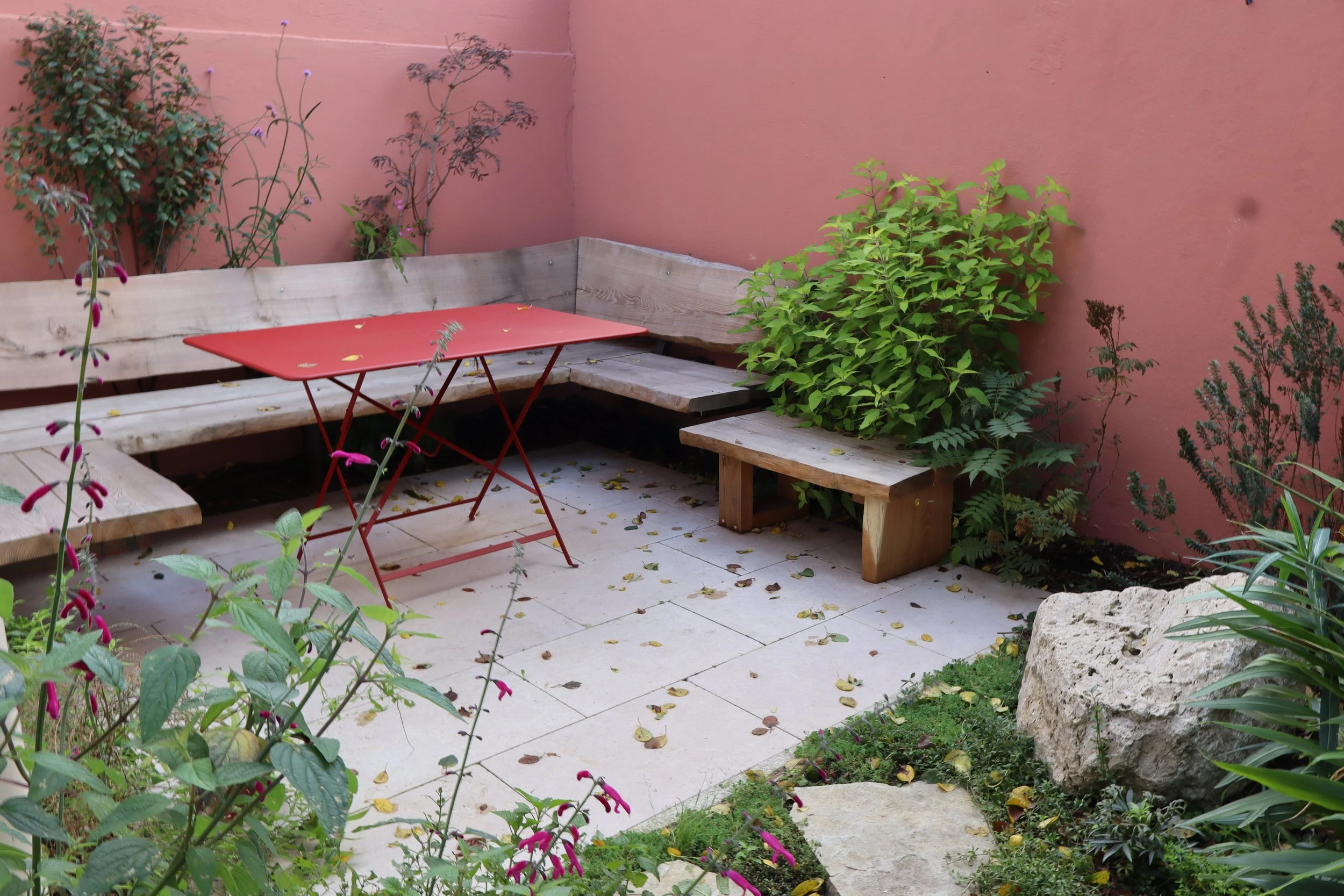 Aménagement d'un patio d'angle par David Simonson avec mur couleur terracota, bancs en bois brut et table rouge