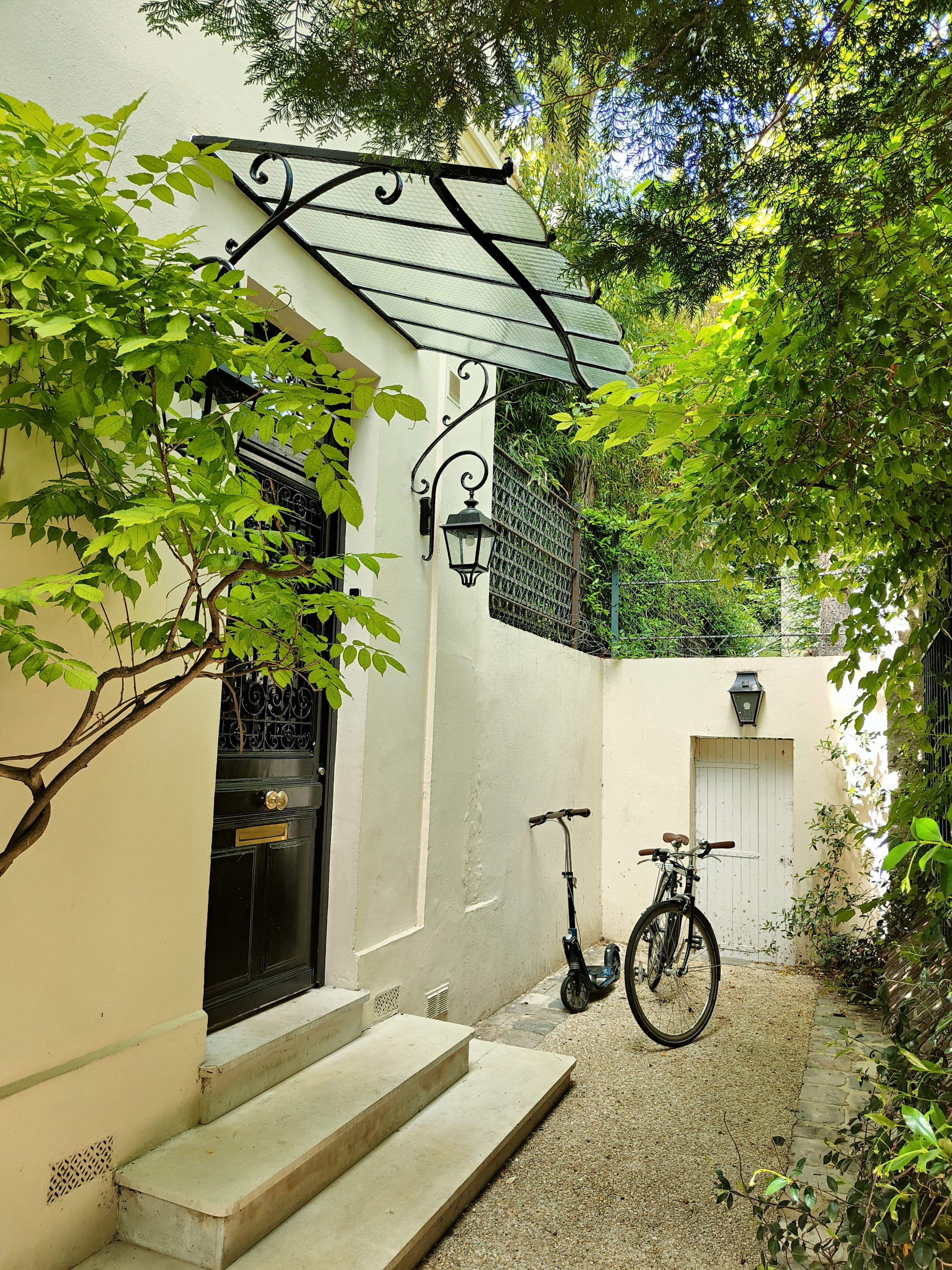 Entrée de maison dans une cour parisienne végétalisée, avec murs clairs, lanternes et grimpantes