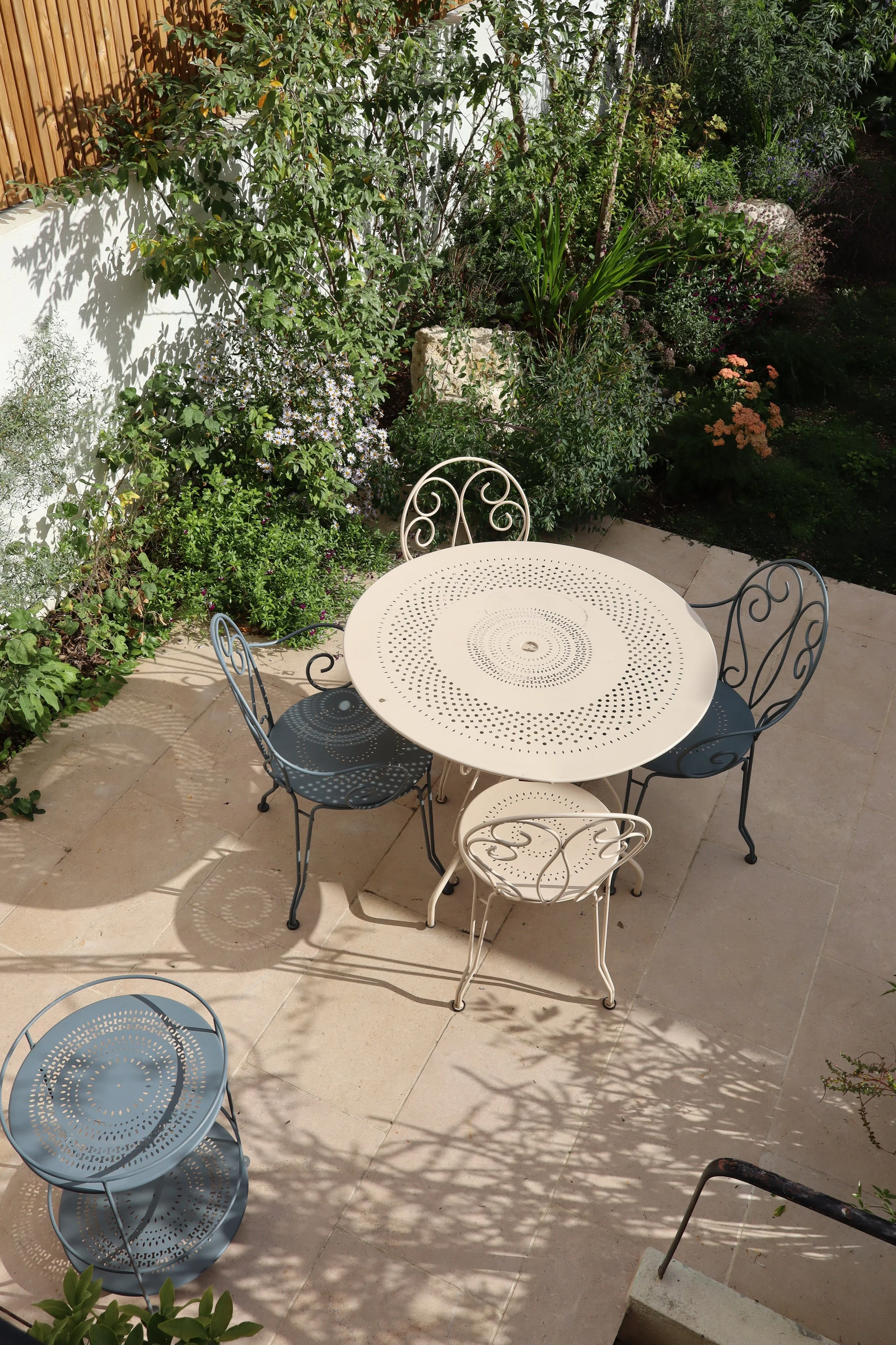 Aménagement d'une terrasse en dalles de pierre claire avec salon de jardin bistrot par David Simonson