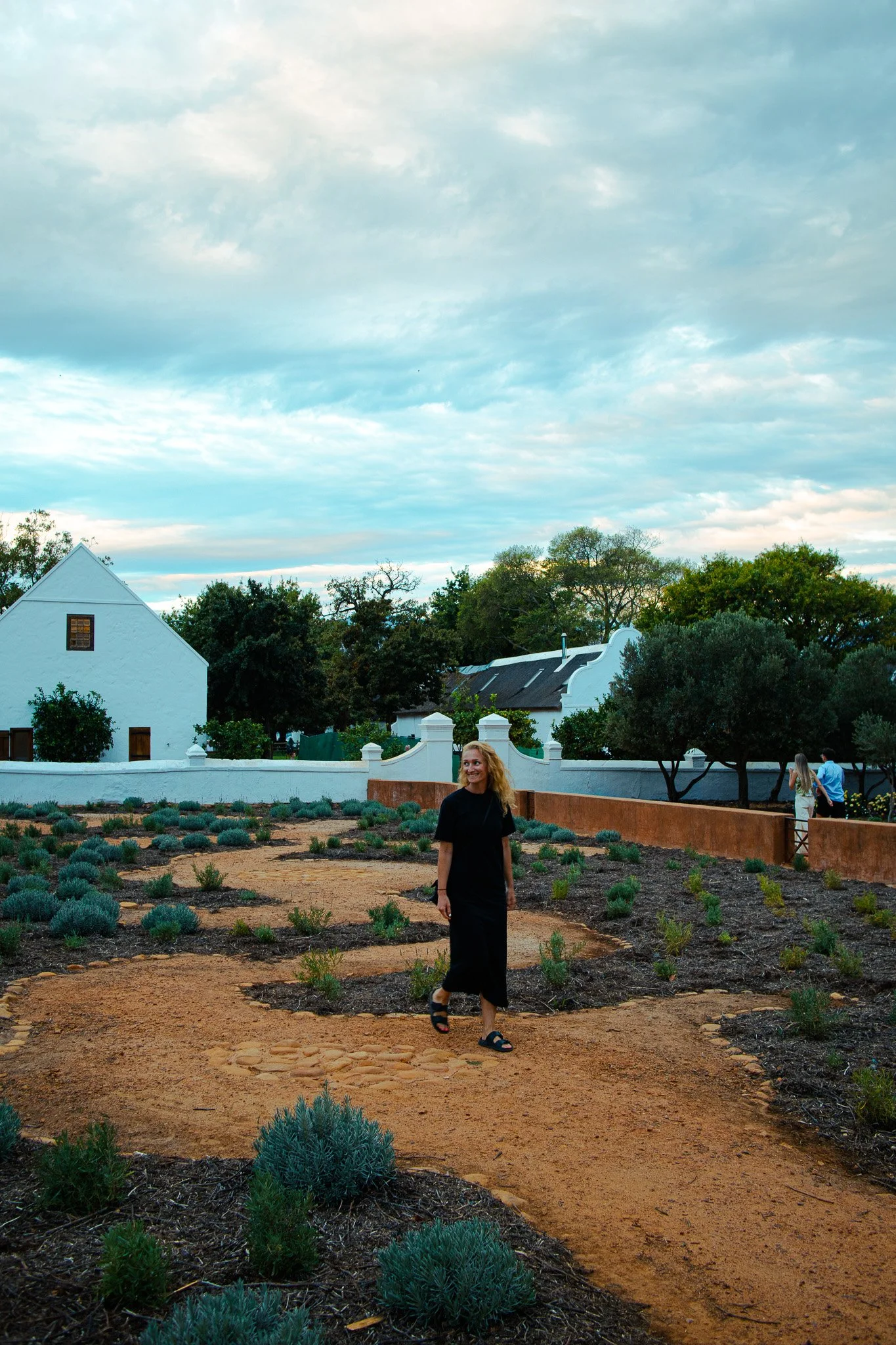 Woman walking on a dirt road with white houses behind