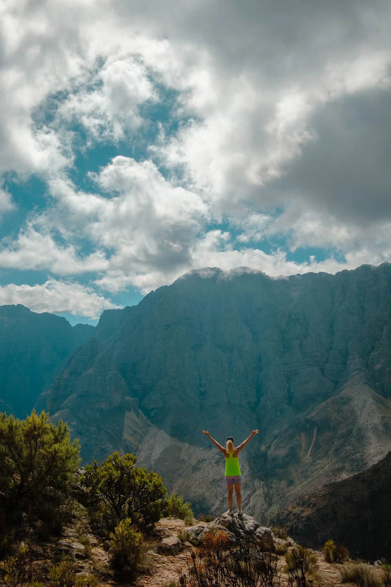 Woman looking over on a mountain range with her arms up in the air