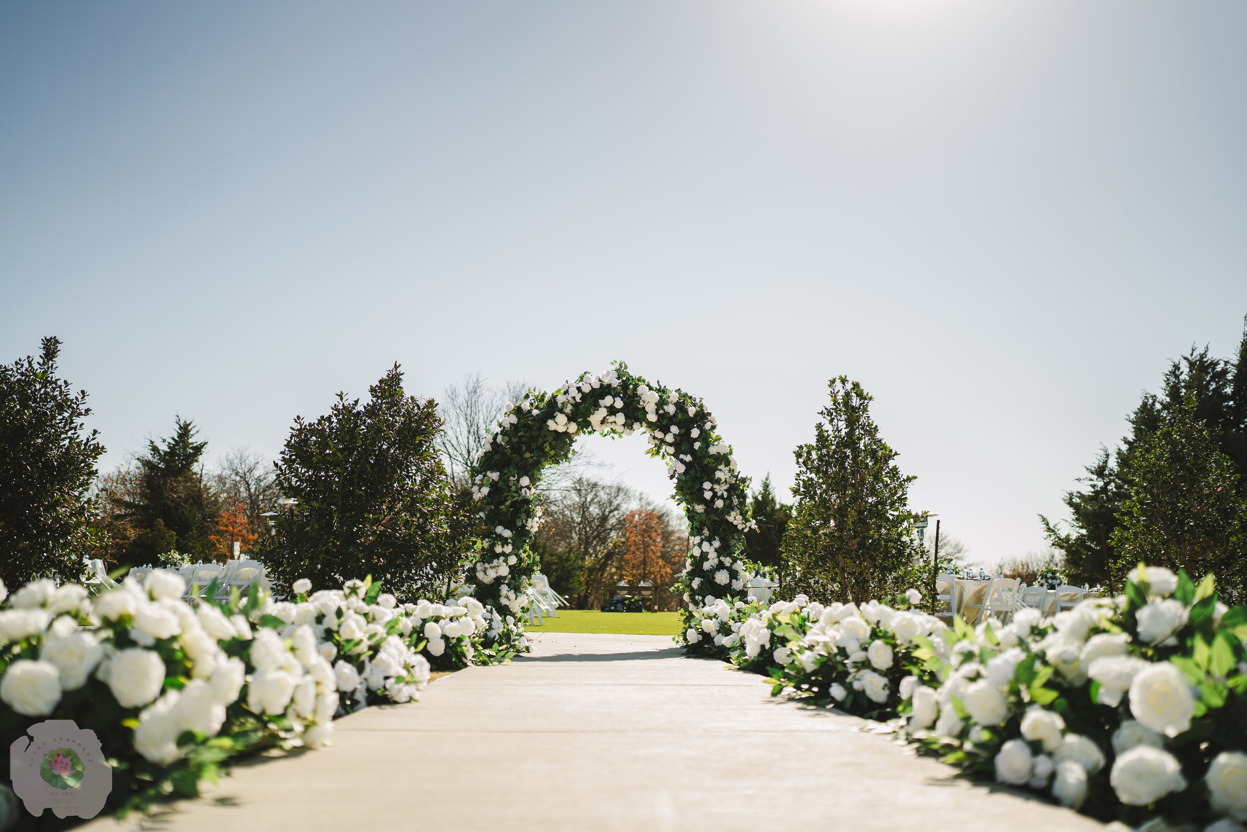 White flowers decorate a walkway leading to an arch.
