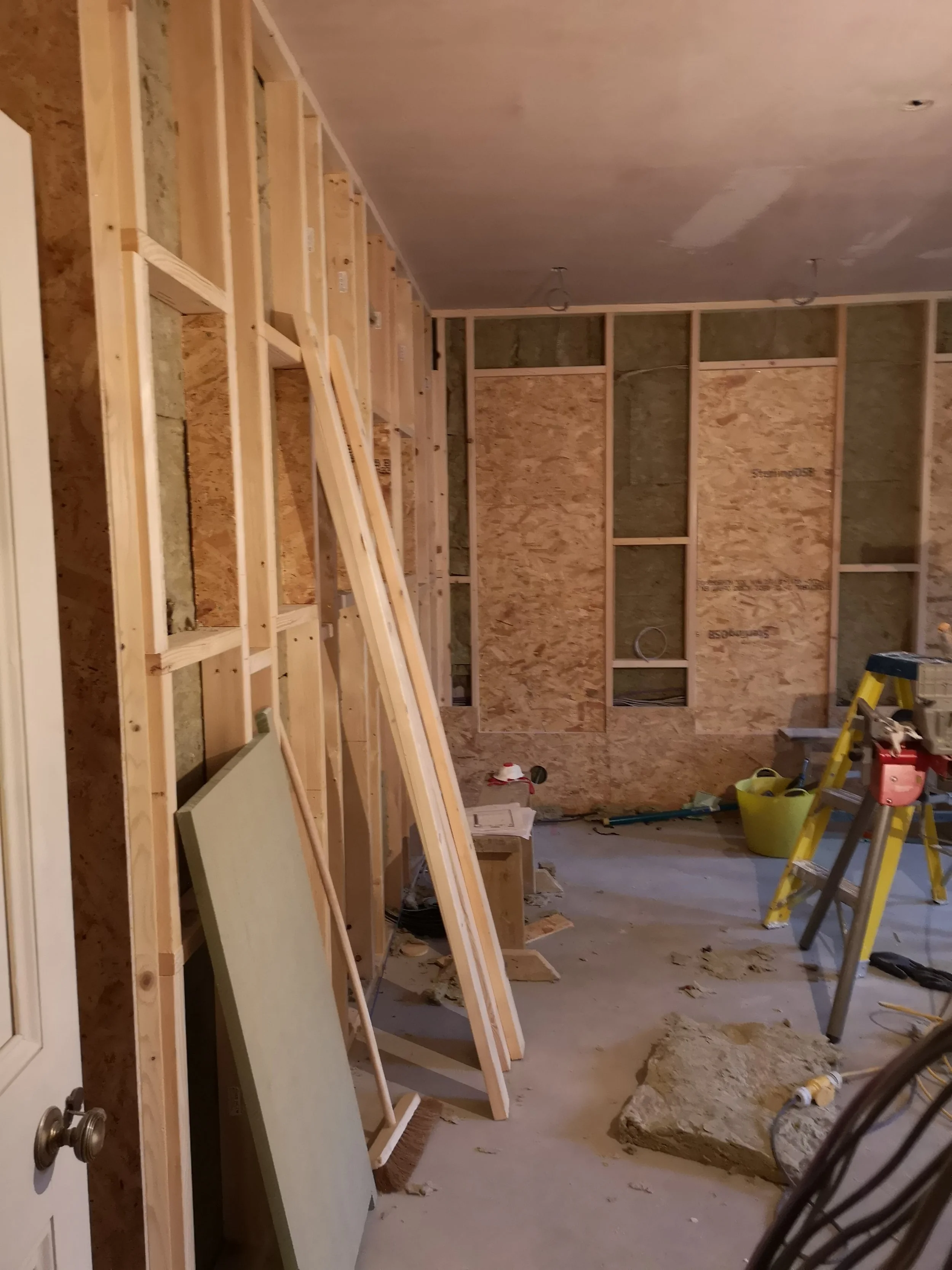Interior view of a room under construction with exposed wooden framing, various construction tools, and materials.