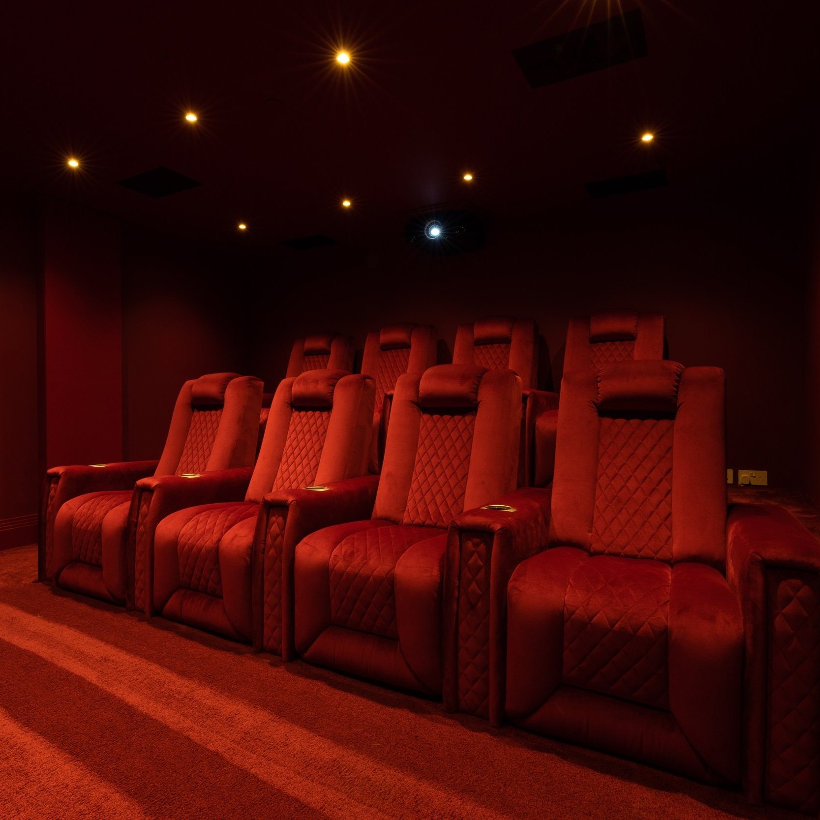 Red movie theater seats in a dark projection room with dim ceiling lights and a projector.
