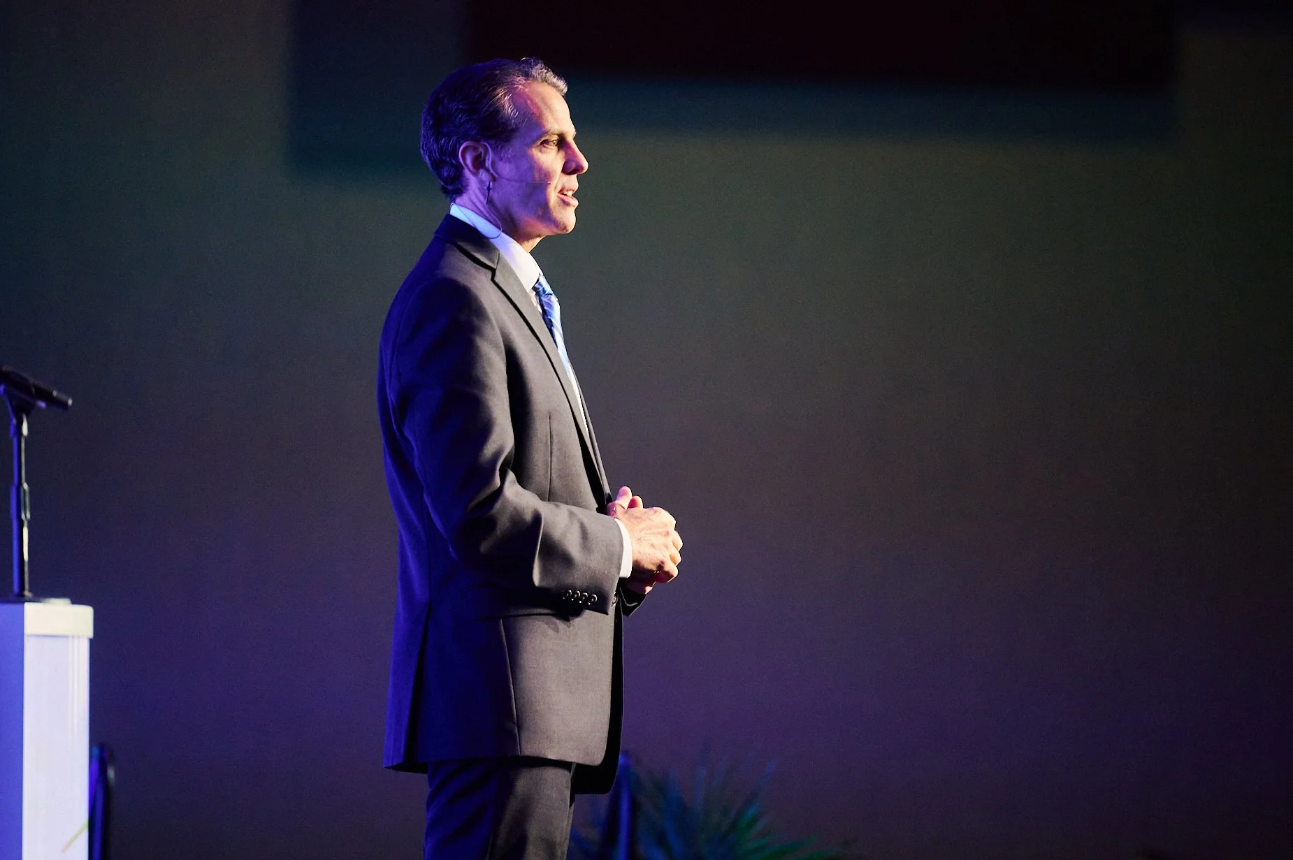 Person in suit speaking on stage with a microphone.