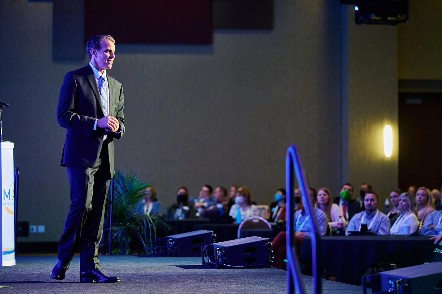 Speaker in suit on stage at conference facing audience