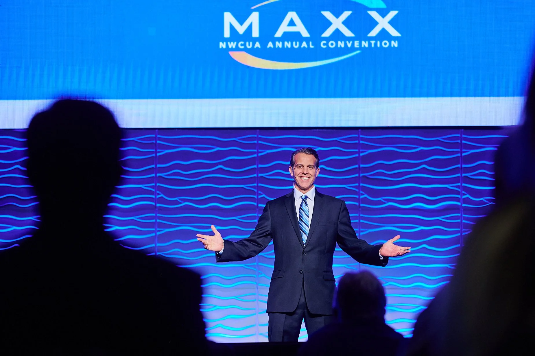 Speaker at NWCUA Annual Convention event on stage with MAXX logo.