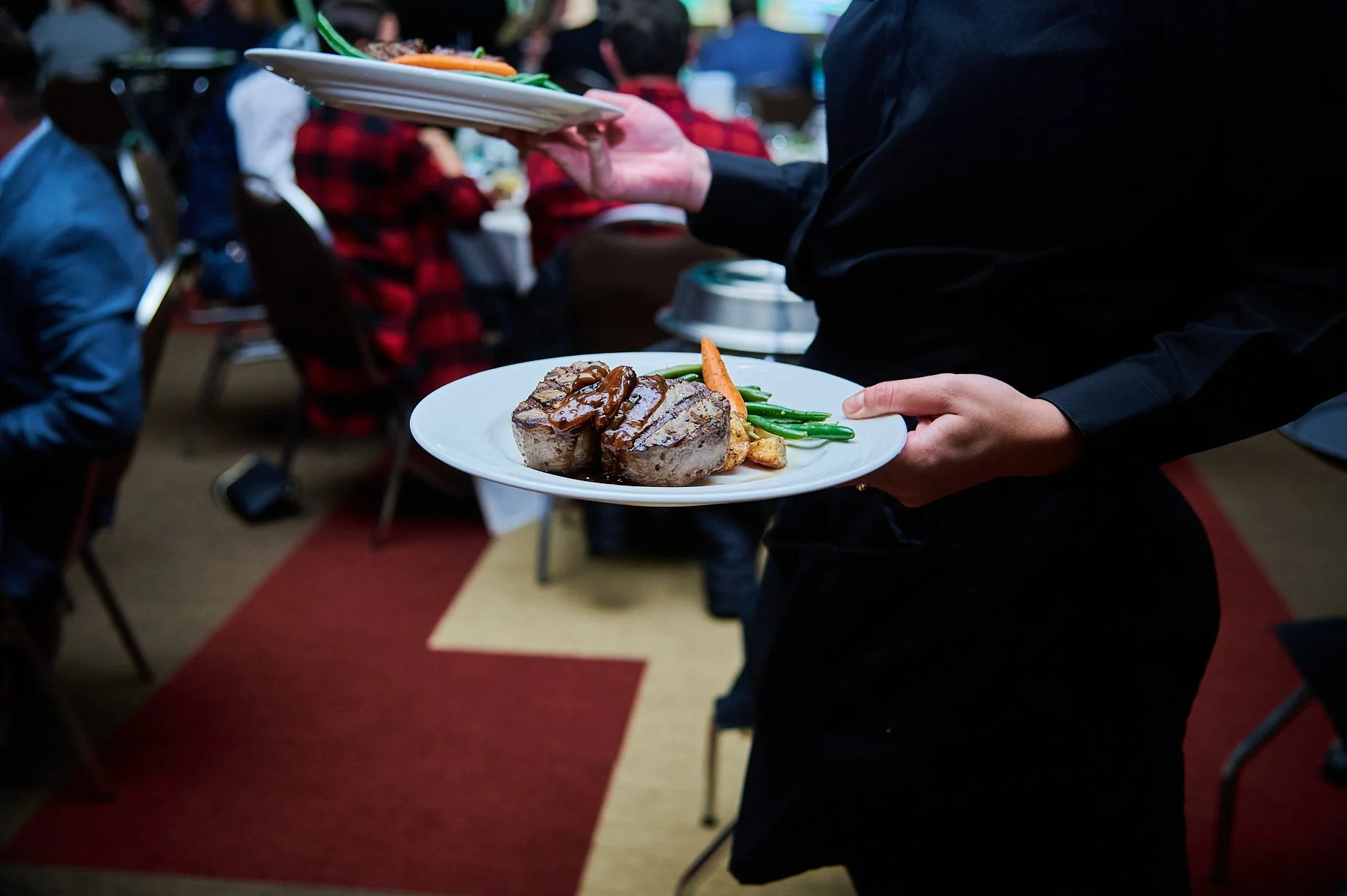 Waiter serving steak dinner with vegetables at an event