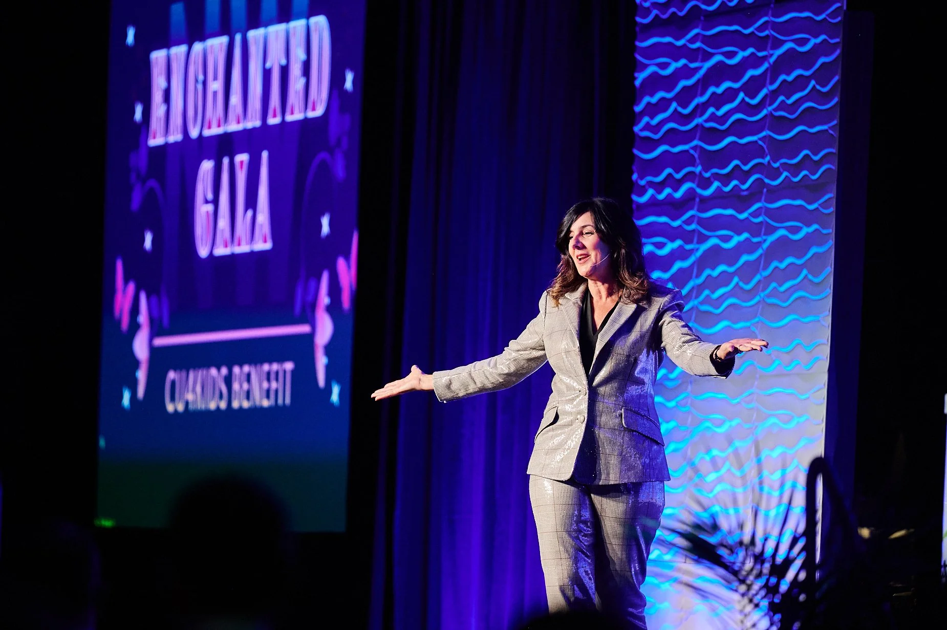 Woman in suit on stage at Enchanted Gala event with blue lighting effect.