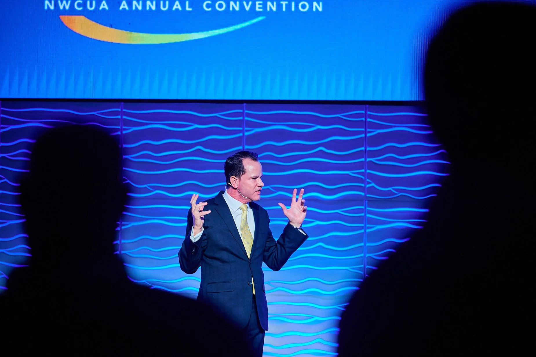 Speaker at NWCUA Annual Convention with blue wave-patterned backdrop