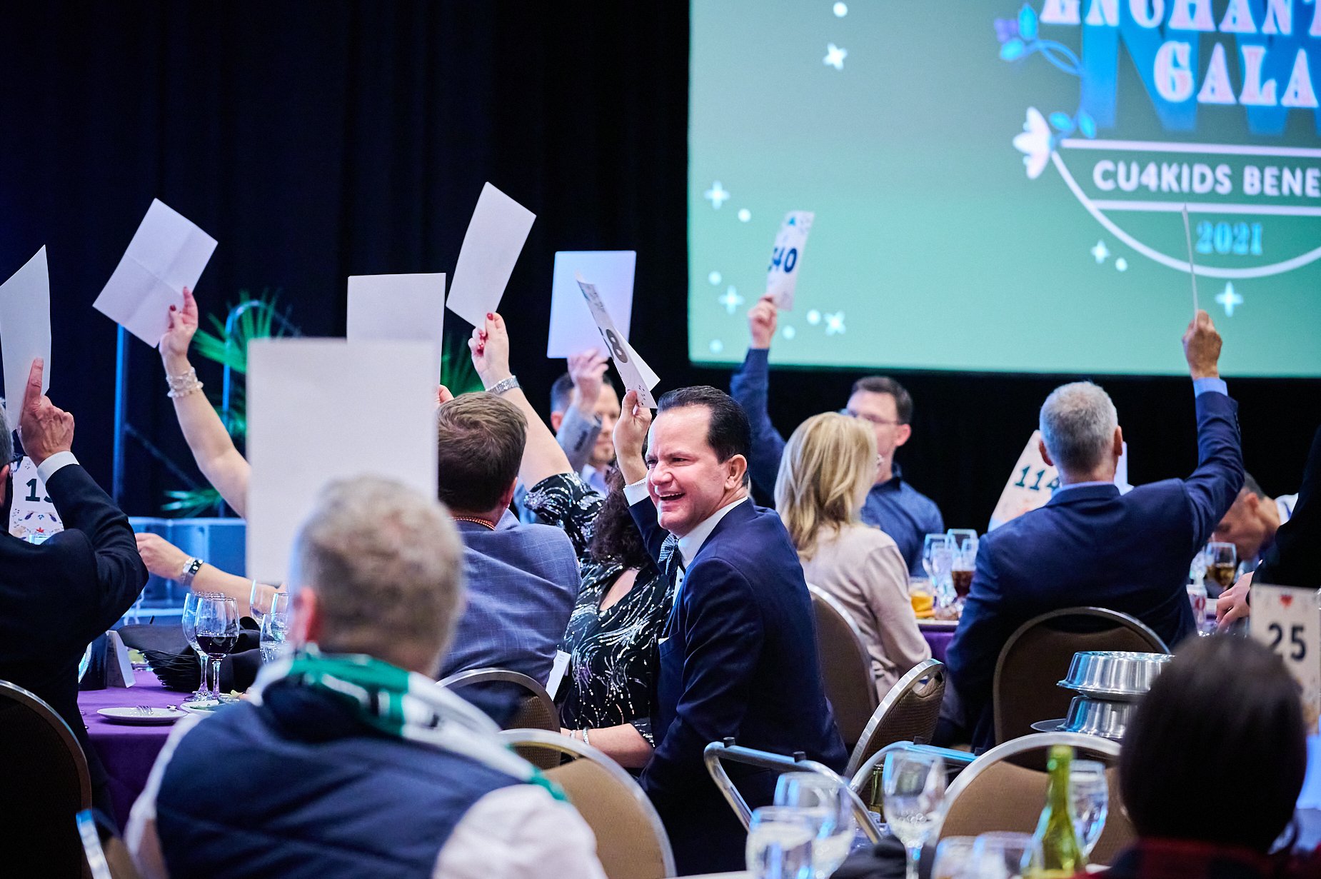 Auction event with participants raising numbered bid cards in a gala setting.