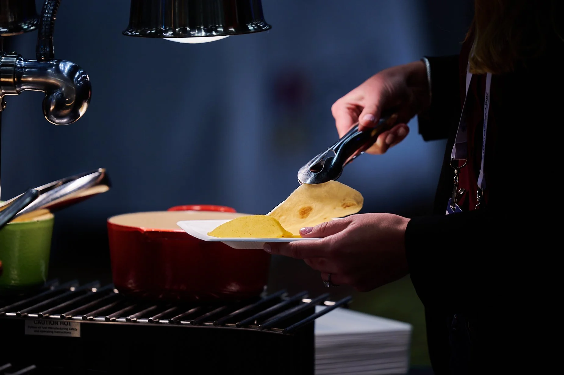Person using tongs to place tortilla on a plate near cooking pots