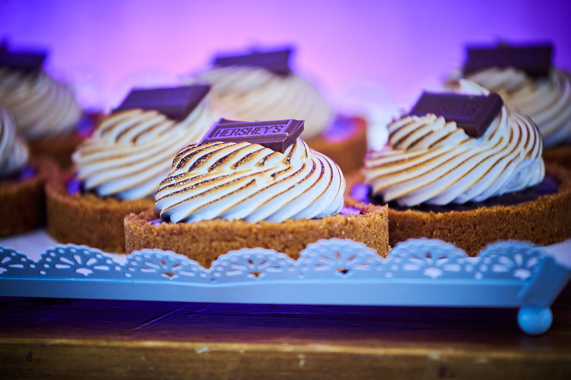 Mini s'mores tarts with toasted meringue and chocolate chunks on a decorative tray.