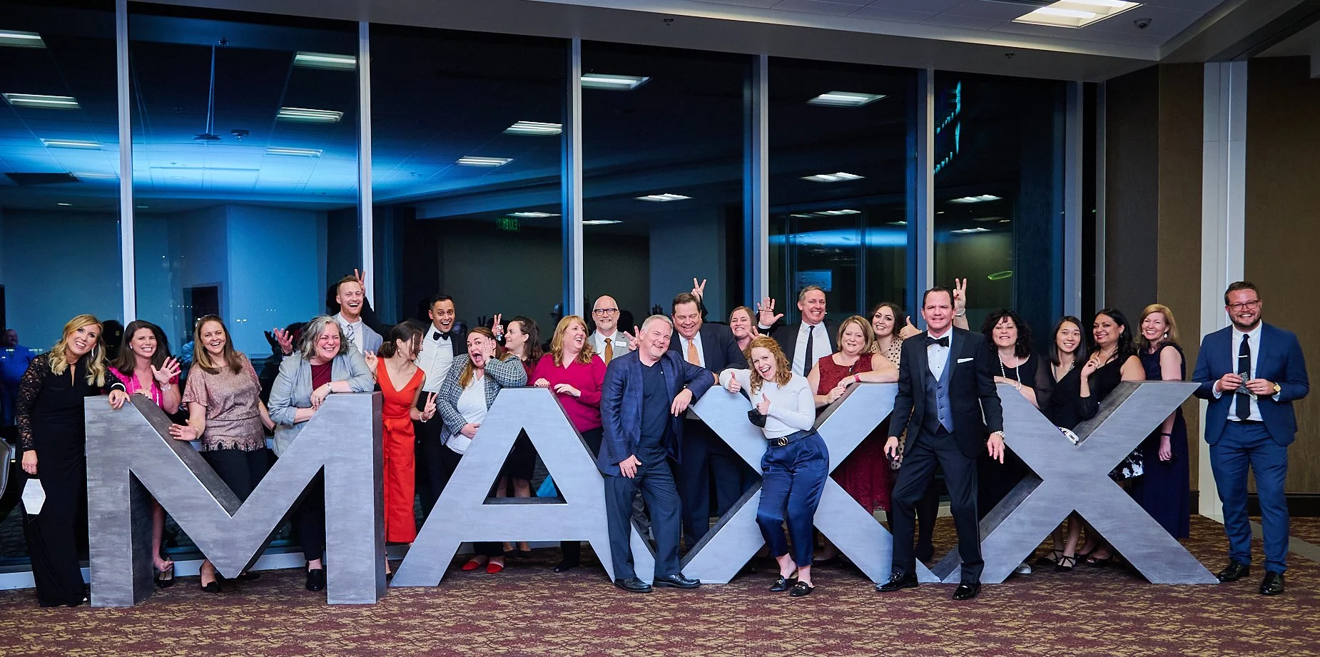 Group of people posing at event with large letters "MAXX" indoors