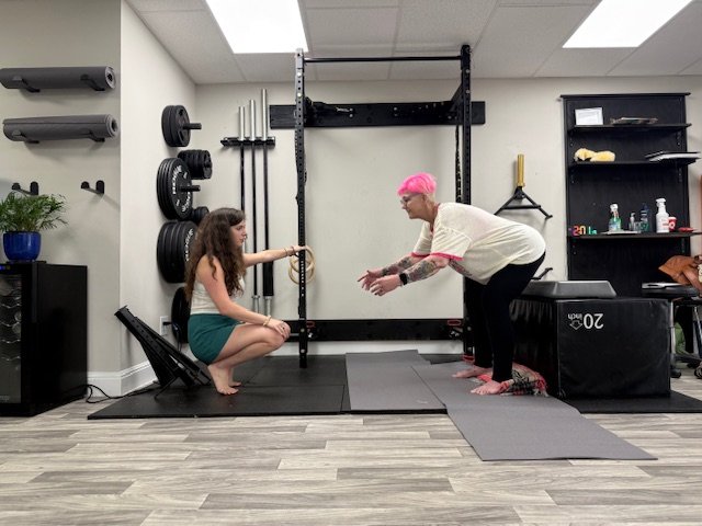 Personal trainer guiding a client through a supported squat in a minimalist strength and mobility studio.