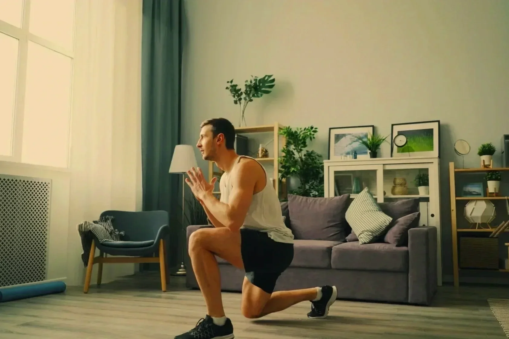 Man practicing a kneeling lunge with hands at chest level in a calm home setting, demonstrating controlled movement and stability
