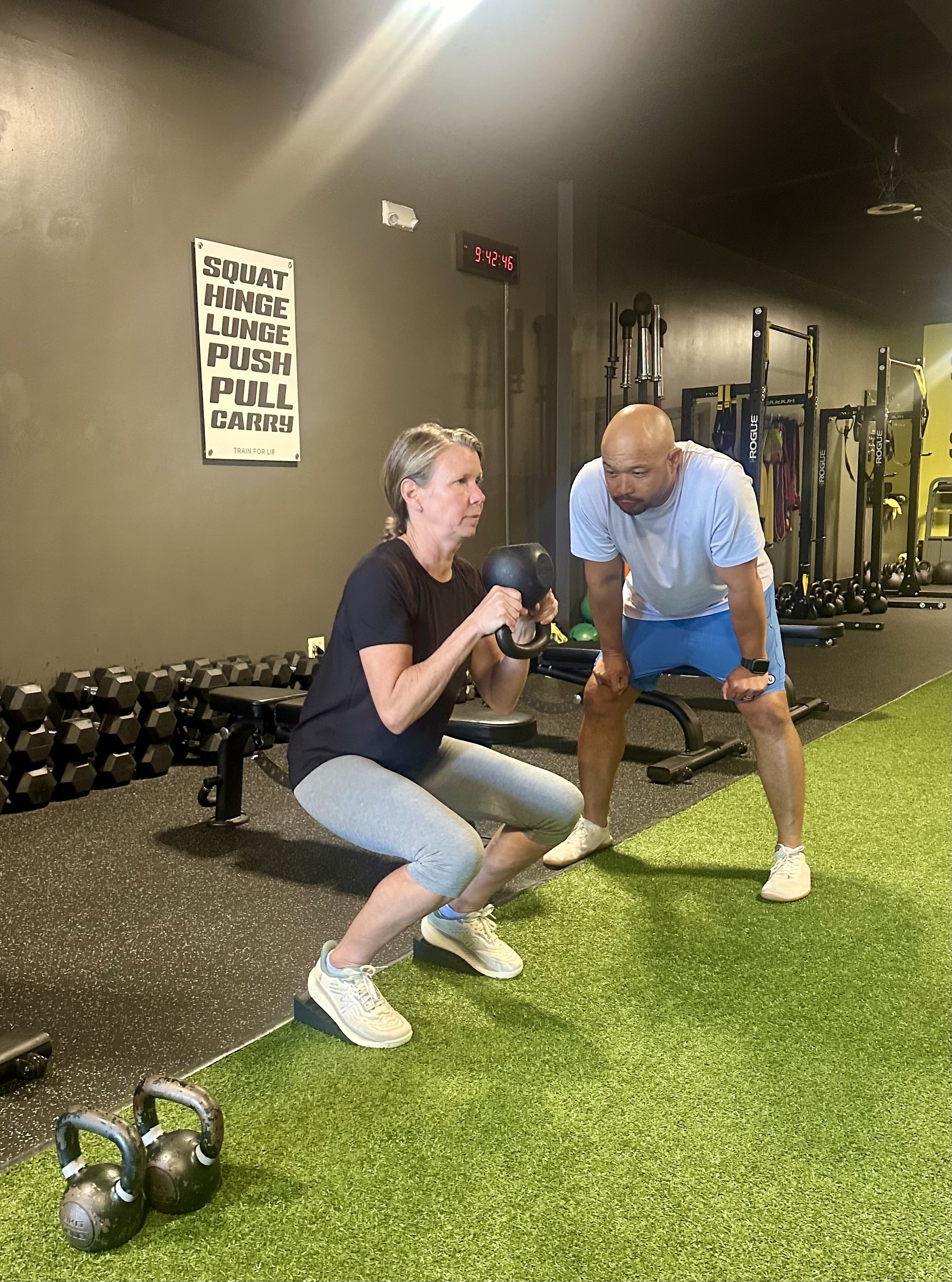 Woman over 40 performing a kettlebell squat with coaching during a strength training session to build muscle and improve healthy aging