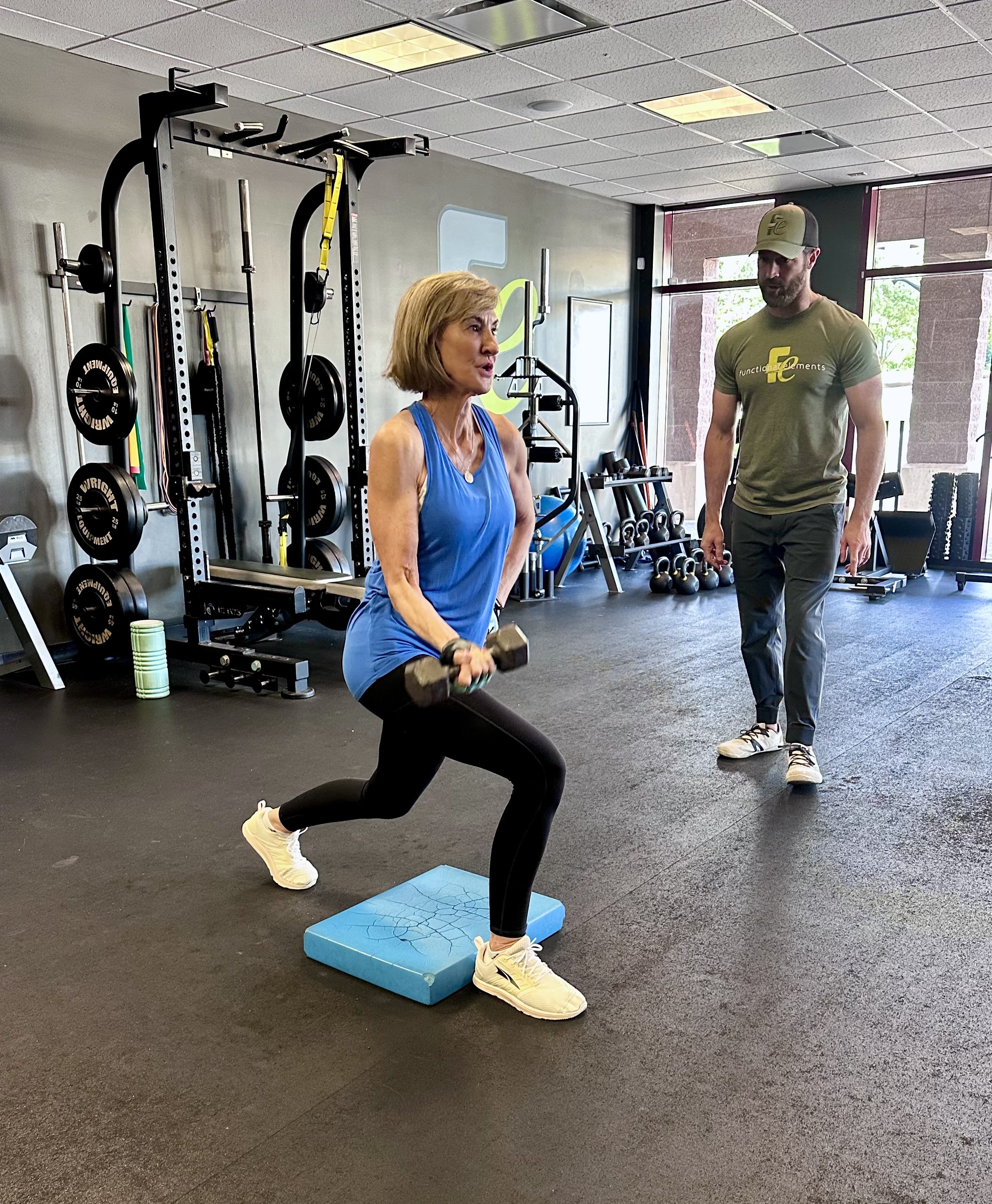 Woman over 40 performing a strength-training exercise with dumbbells while working with a coach to improve balance, strength, and healthy aging