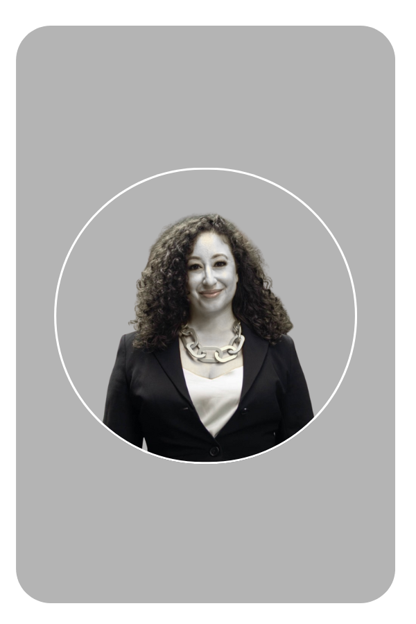 A woman with curly hair smiling, wearing a black blazer, white top, and a large chain necklace against a black background.