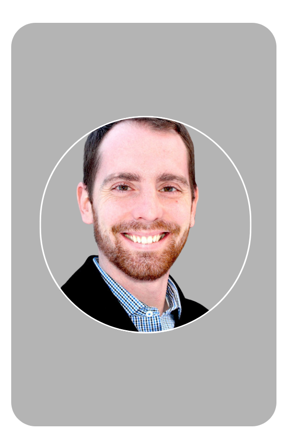 Smiling man with a beard in a checkered shirt and blazer on a dark background.