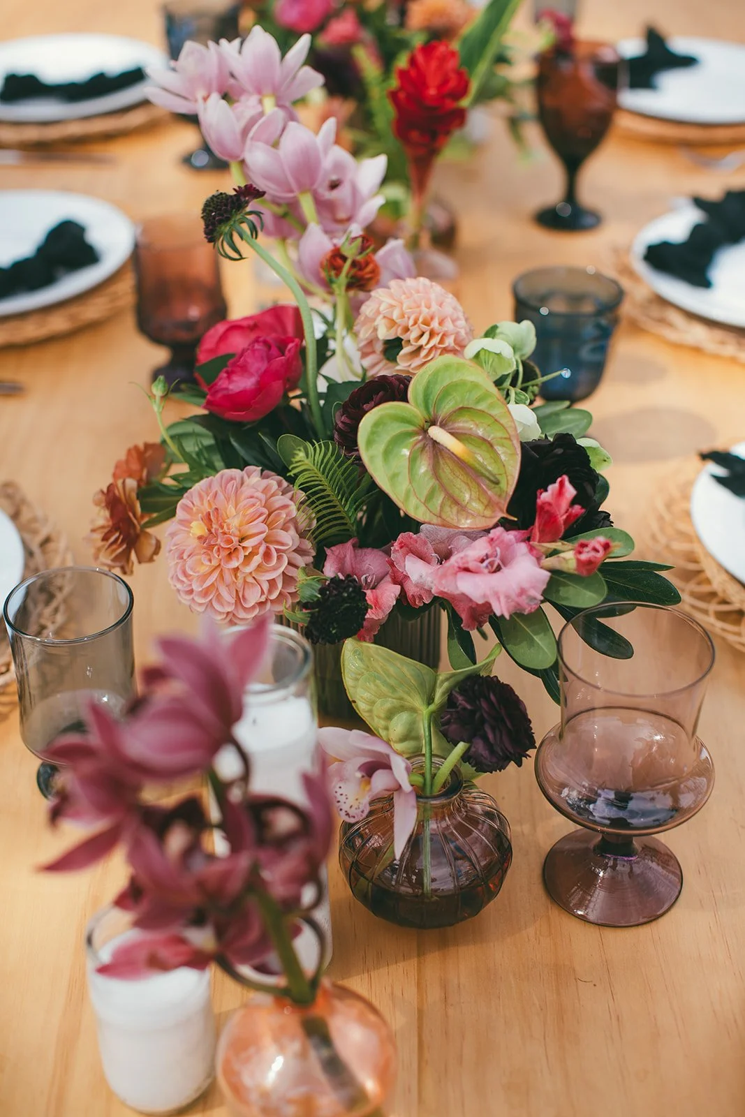 Closeup on a moody-tropical centerpiece of anthurium and orchids, plus dahlias and coral charm peonies.