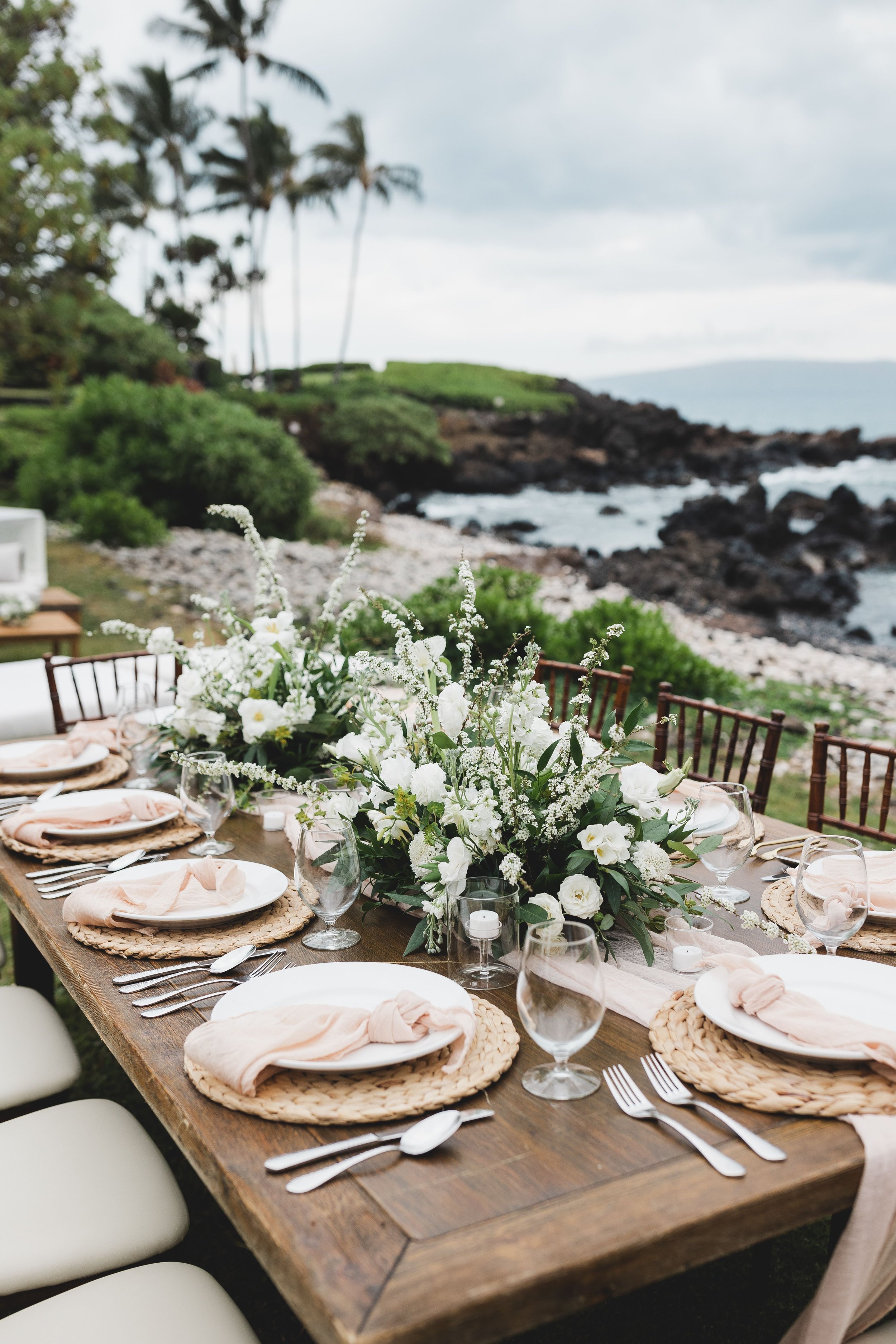 An outdoor tropical wedding reception before the ocean and lava rock formations in the distance