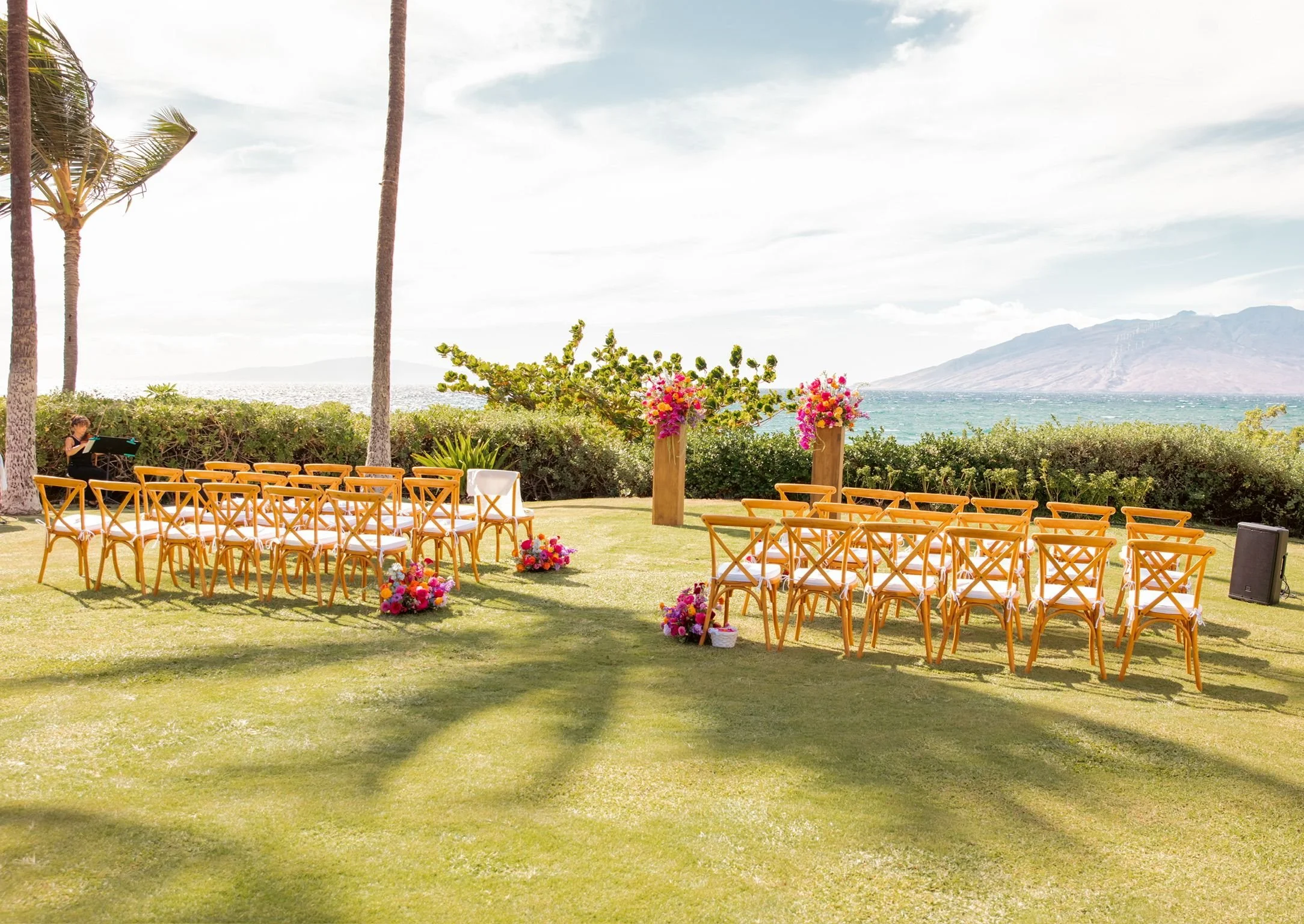 A beachside tropical outdoor wedding on the grass, with bright fuchsia florals