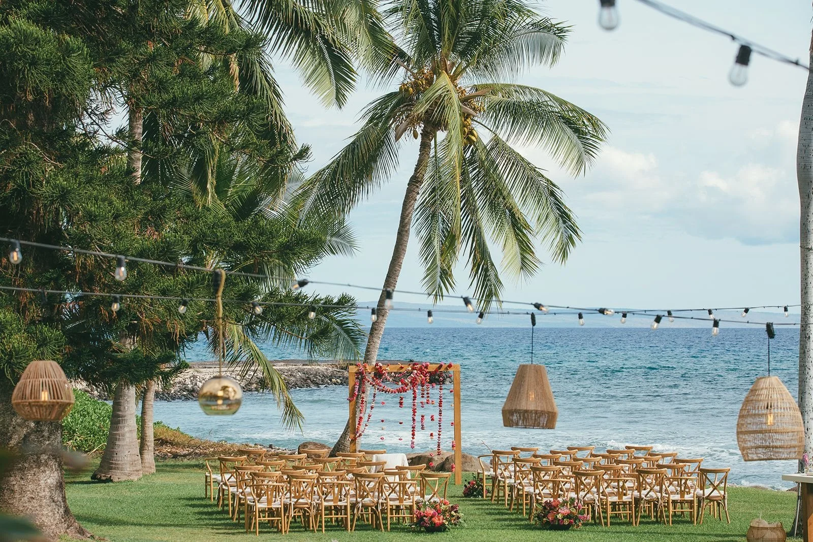 A beachside wedding ceremony on the grass, with a square wooden wedding arch draped with strung carnations