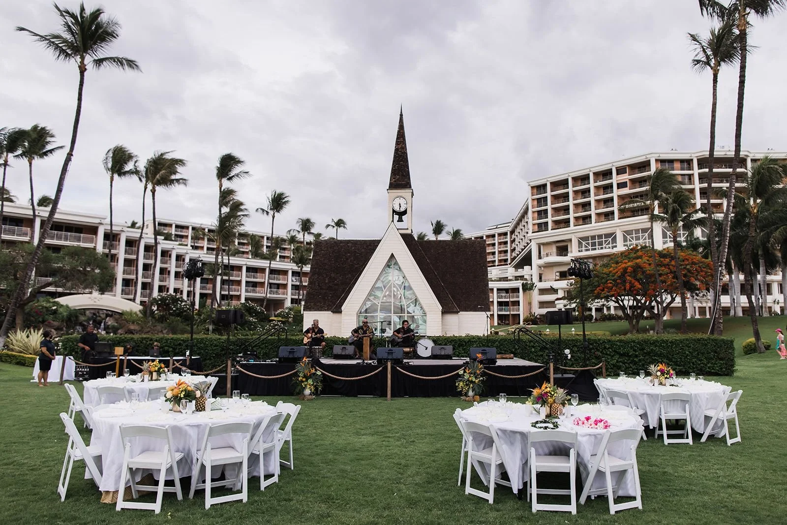An outdoor resort wedding reception with a music stage and small chapel in the background