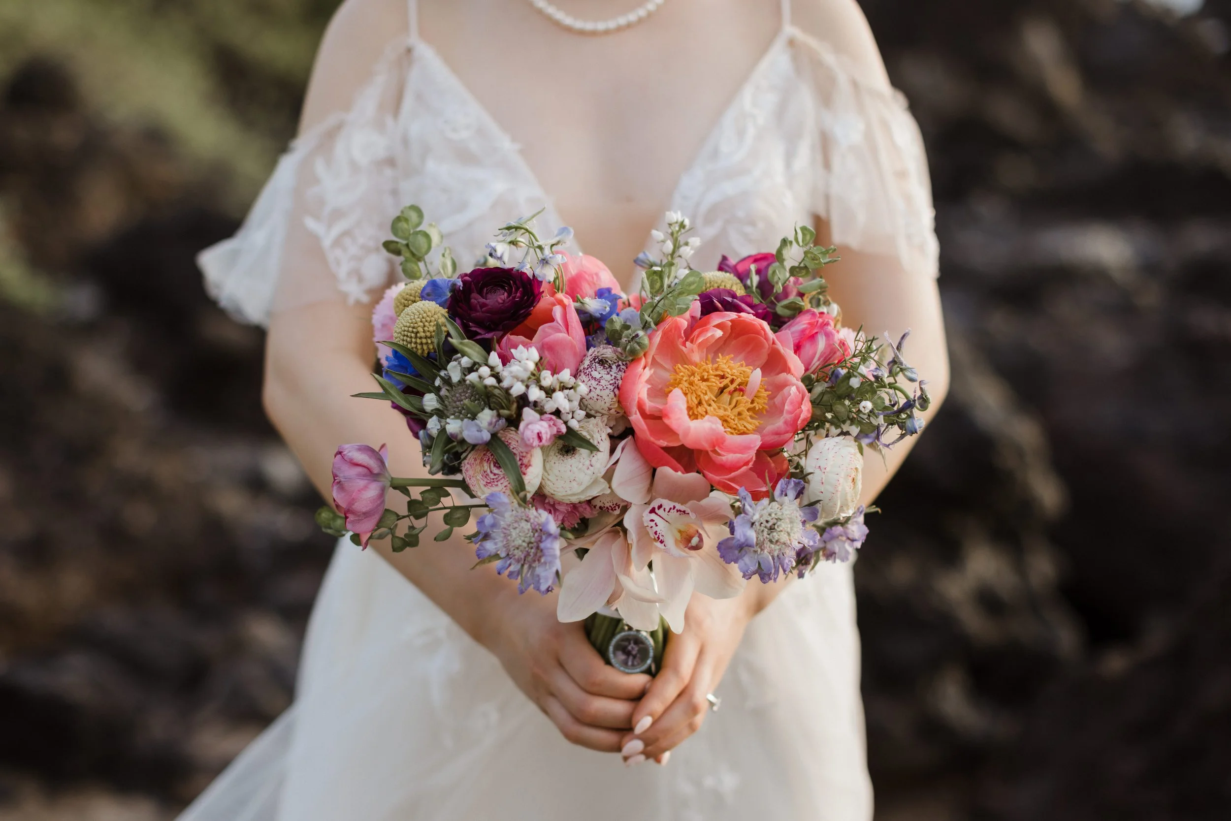 A pink and purple bridal bouquet with coral charm peonies, tulips, ranunculus, orchids, scabiosa, and more.