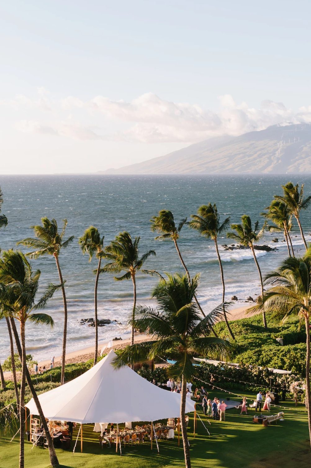 An outdoor tropical wedding on the grass by the beach, with the curve of the Maui island in the distance