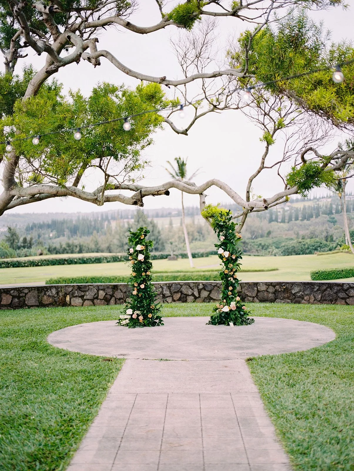 An outdoor wedding ceremony with a deconstructed flower arch before a lush green view.
