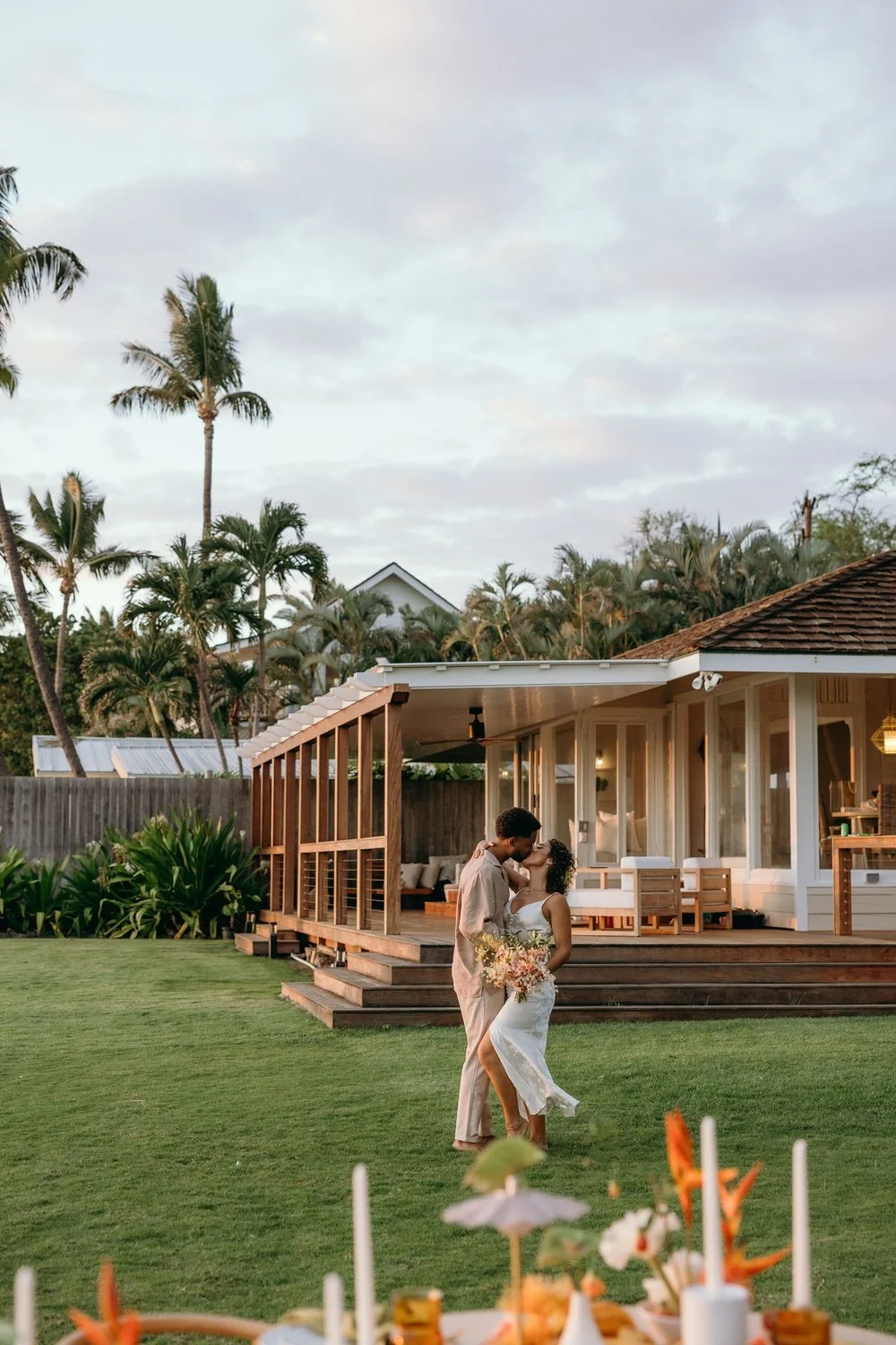 A bride and groom kissing on the lawn beside a chic, light-filled wedding venue home