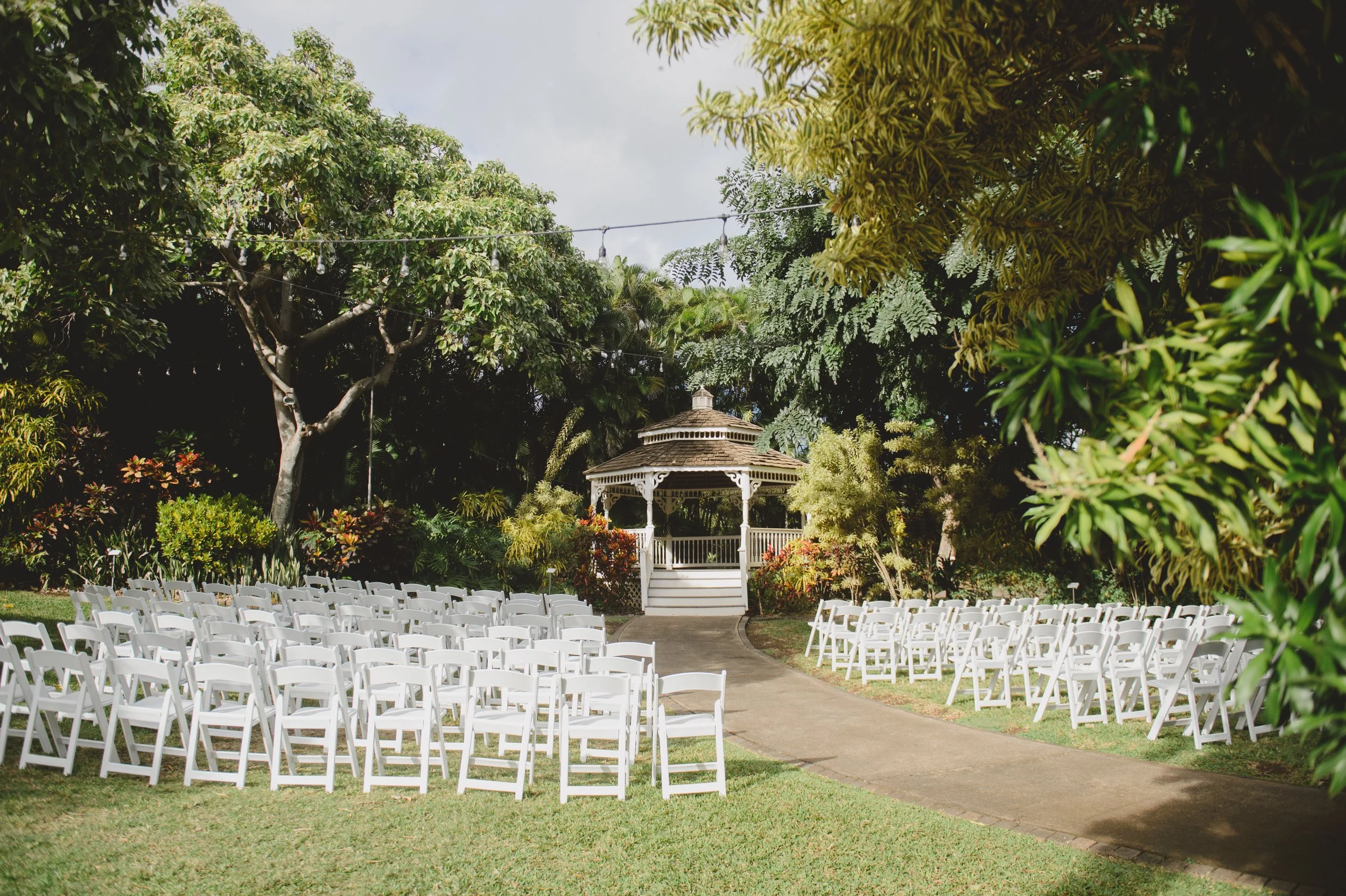 An outdoor wedding reception in a mango grove before a garden gazebo.
